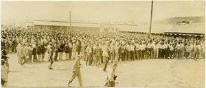 Hundreds of Men in Civilian Clothing Standing in Lines Waiting to Enter Buildings